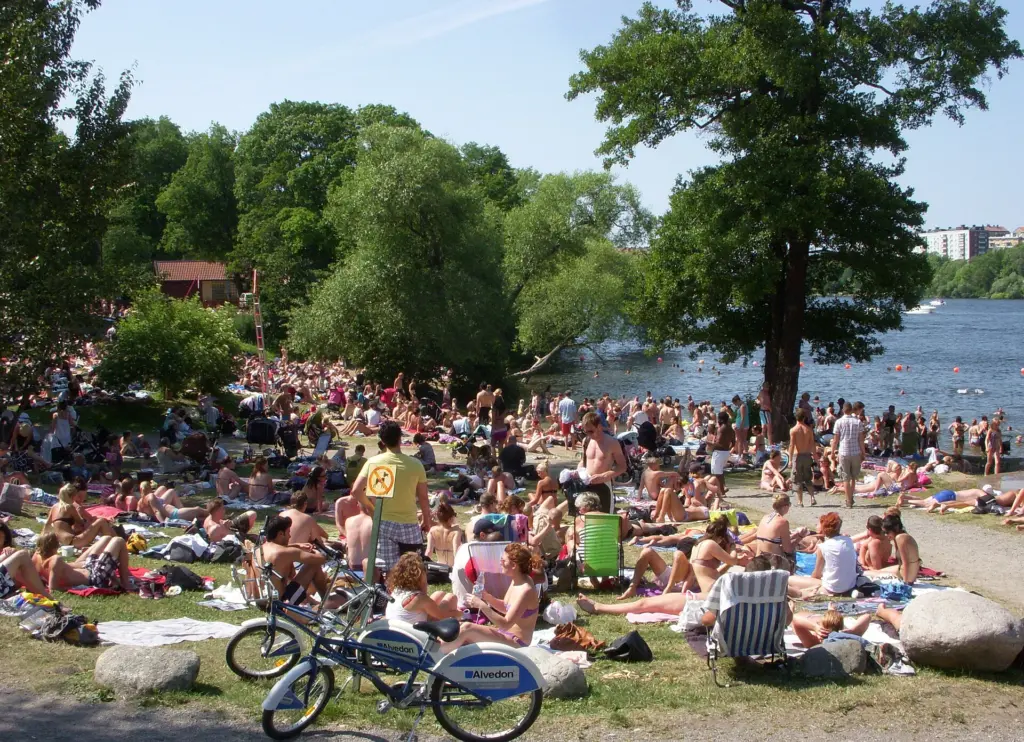 Badande och solbadare på gräsmattan vid Långholmsbadet
